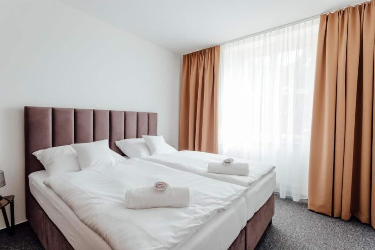 Habitación de hotel con dos camas, un ventanal con cortinas y un cabecero moderno.