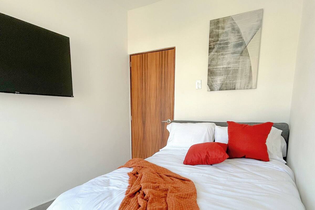 Un dormitorio con una cama, un televisor fijado a la pared y una puerta.
