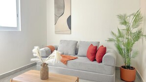 Een woonkamer met een grijze bank, een houten salontafel, een vaas met veren, een potplant en een groot abstract schilderij aan de muur.