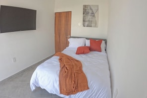 Un dormitorio con cama, una puerta de madera, un televisor montado en la pared y un cuadro.