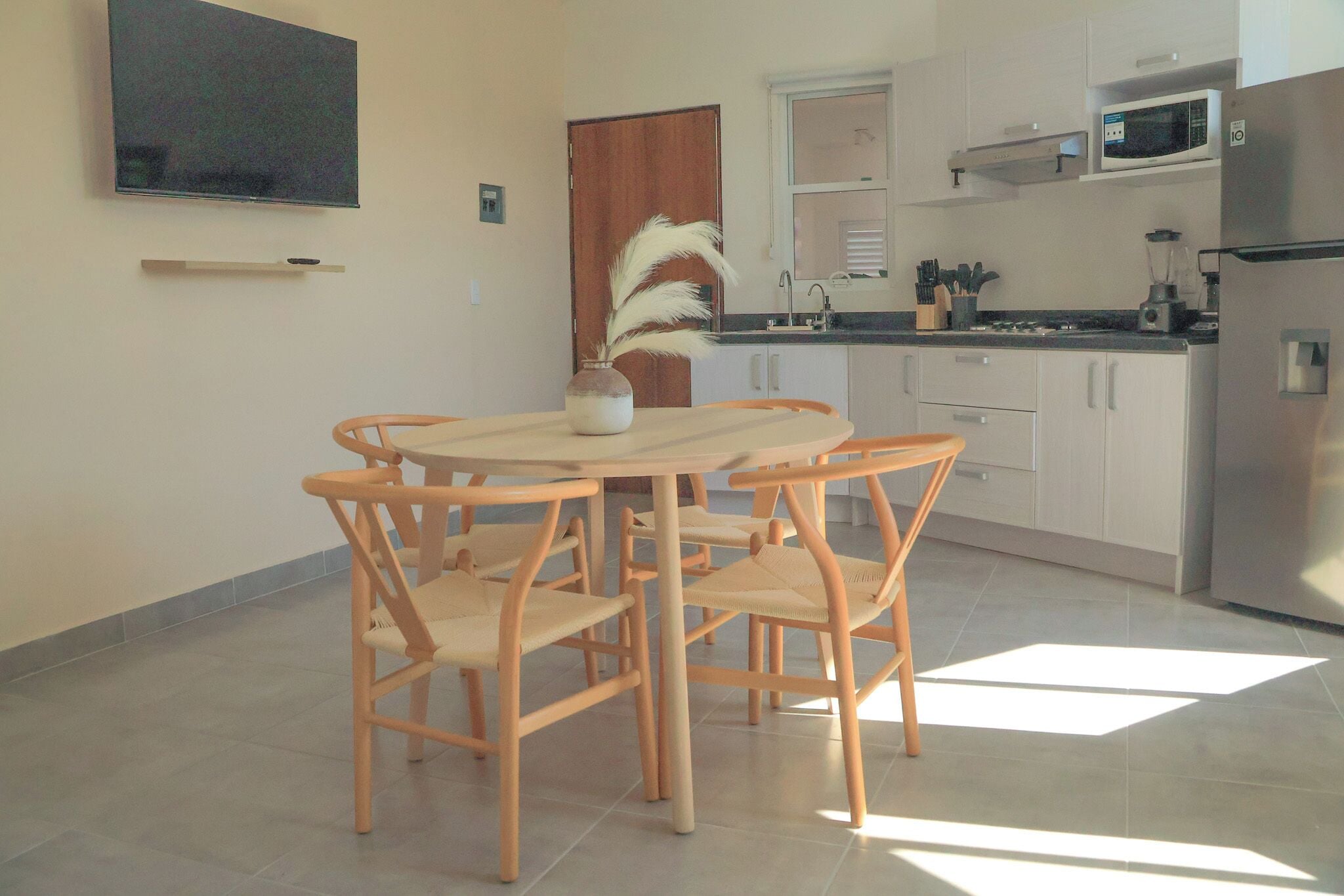 Een moderne keuken met witte kasten, een roestvrijstalen koelkast, een magnetron en een eethoek met een ronde tafel en houten stoelen.