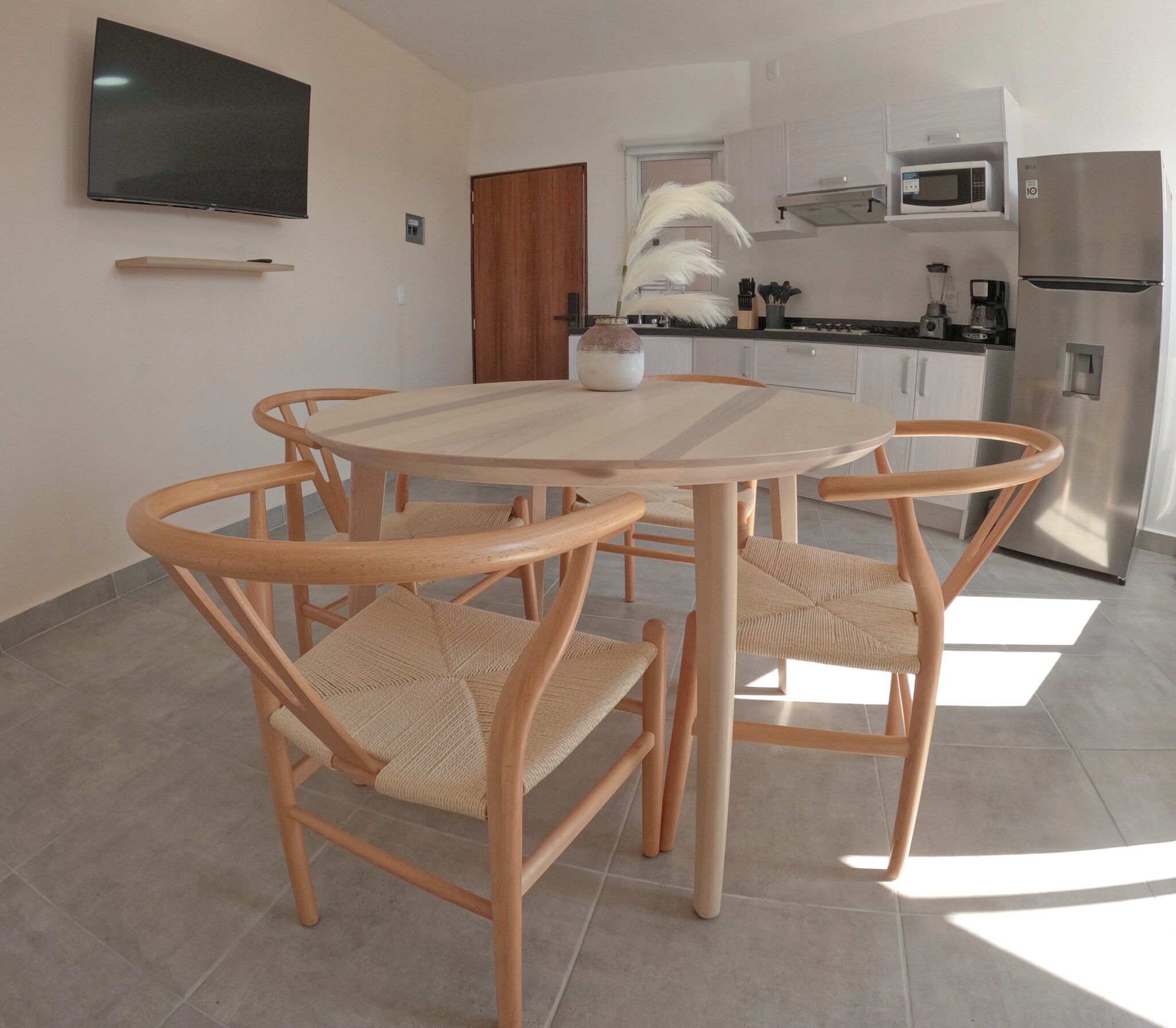 Cocina moderna con refrigerador de acero inoxidable, microondas y estufa. Hay una mesa de madera redonda con cuatro sillas.