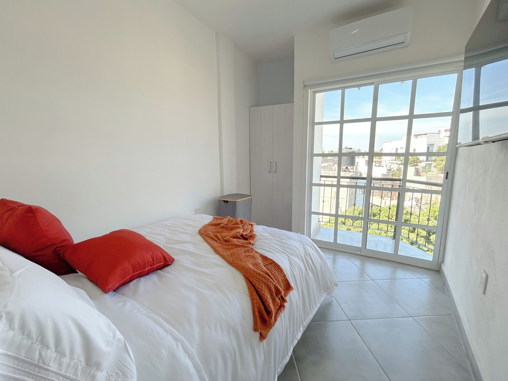 A bedroom with a bed, red pillows, a white blanket, a window with a view, and a small table.