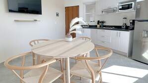 Een moderne keuken met witte kasten, een flatscreen televisie boven de aanrecht en een eethoek met een ronde tafel en rieten stoelen.