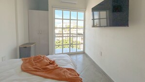 Een slaapkamer met een bed, een oranje deken, een garderobe, een televisie aan de muur en een balkon met uitzicht.