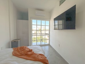 A bedroom with a bed, an orange blanket, a wardrobe, a TV on the wall, and a balcony with a view. - El Pitillal (Puerto Vallarta)