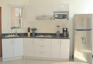 Una cocina con armarios blancos, microondas, cocina a gas, cafetera y refrigerador.