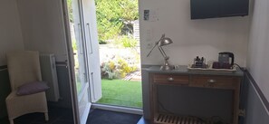 Habitació amb una porta corredissa que dona a un jardí, un escriptori amb una làmpada, una cafetera i una cadira amb coixí.