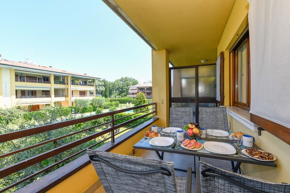 Ein Balkon mit Frühstückstisch, mit Blick auf einen Garten und weitere Gebäude.