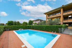 Ein rechteckiger Pool mit weißem Rand, umgeben von einer Pflasterterrasse.