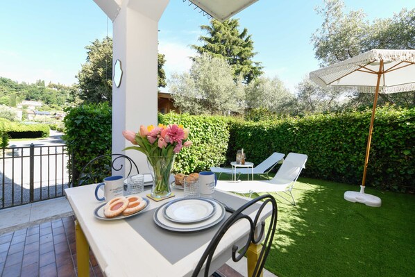 An outdoor patio with a table set for two, a flower vase, and a white umbrella. - MGH- AMAI Small Holiday Cottage (Manerba del Garda)