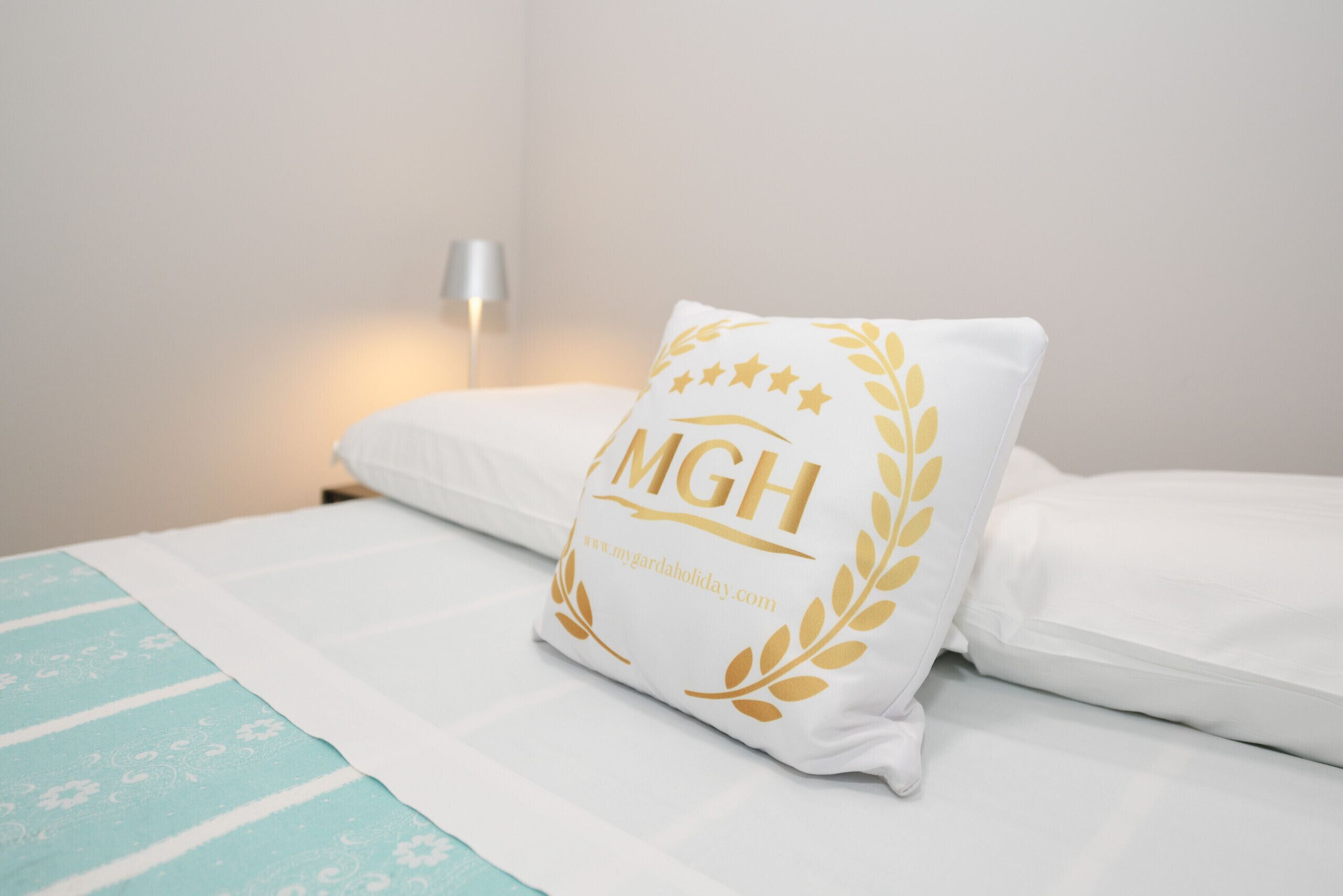 Ein Bett mit weißer Bettwäsche und einem Kissen mit goldenem Emblem und Schriftzug.