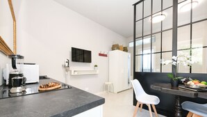 A modern kitchen with a black countertop, white cabinets, a coffee machine, and a dining area with a table and chairs. - MGH- AMAI Small Holiday Cottage (Manerba del Garda)