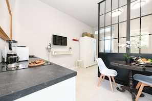 A modern kitchen with a black countertop, white cabinets, a coffee machine, and a dining area with a table and chairs. - MGH- AMAI Small Holiday Cottage (Manerba del Garda)