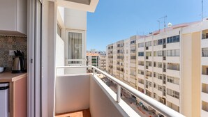 A balcony with a view of a multi-story residential building, a window with curtains, and a kitchen area with a kettle and utensils. - Acolhedor T2 em Armação de Pêra by Lovelystay (Armacao de Pera)