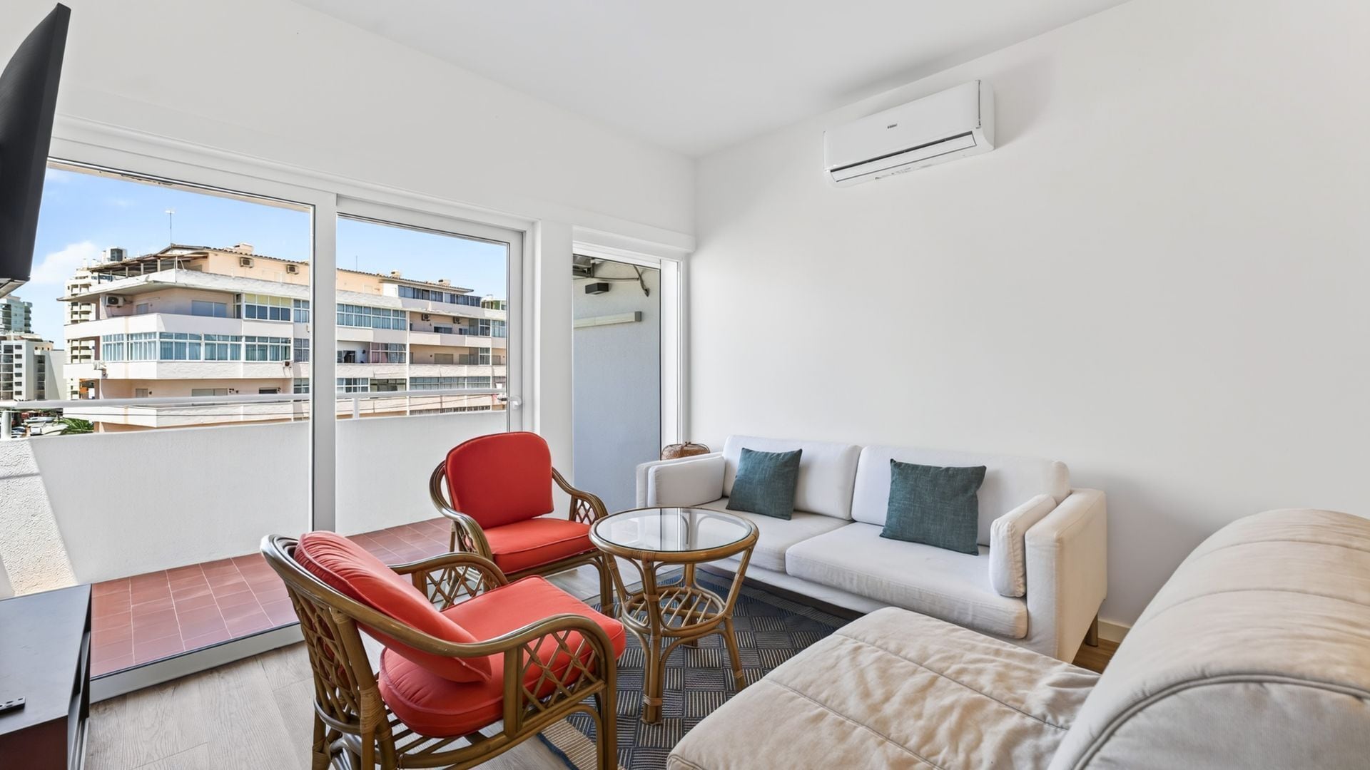 A modern living room with a sofa, two chairs, a small table, and a view of the city through large windows.
