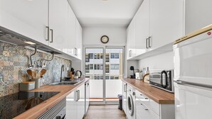 A modern kitchen with white cabinets, a patterned backsplash, and a view of a building through a glass door. - Acolhedor T2 em Armação de Pêra by Lovelystay (Armacao de Pera)
