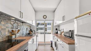 Eine moderne Küche mit weißen Schränken, einer ornamental gestalteten Spritzschutzleiste und Blick auf ein Gebäude durch eine Glastür.