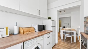 A compact kitchen with a microwave, toaster, and washing machine. There is a dining area with a table and chairs. - Acolhedor T2 em Armação de Pêra by Lovelystay (Armacao de Pera)