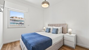 A bedroom with a bed, bedside tables, a window, and a view of buildings outside. - Acolhedor T2 em Armação de Pêra by Lovelystay (Armacao de Pera)