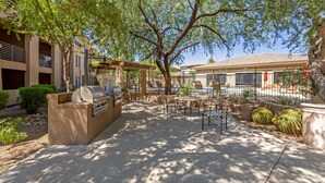 Eine Außenpatio-Terrasse mit Grill, Sitzgelegenheit und Pool im Hintergrund.
