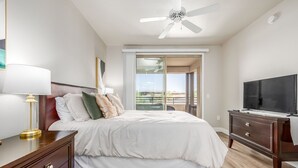 Ein Hotelzimmer mit Bett, Fernseher, Deckenventilator, einer Schiebetür zum Balkon und einer Holzkommode.