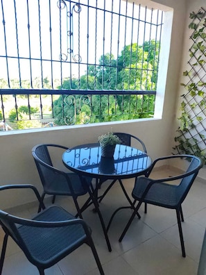 A balcony with a round table and four chairs, a potted plant, and a view of greenery. - sembrador v manzana A edificio 9 (Santo Domingo Este)