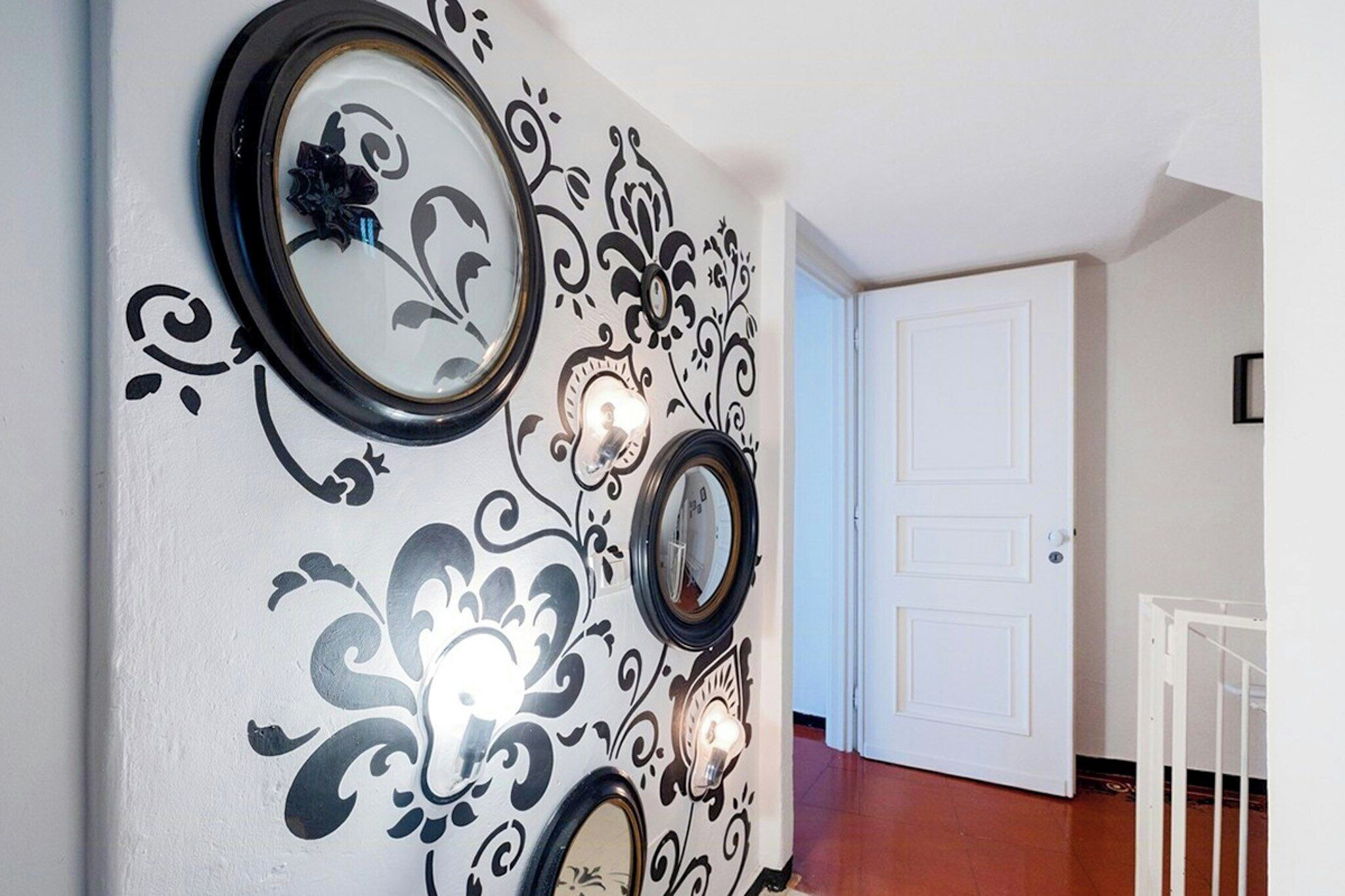 Un pasillo con arte decorativo en las paredes, una puerta blanca y una barandilla blanca.