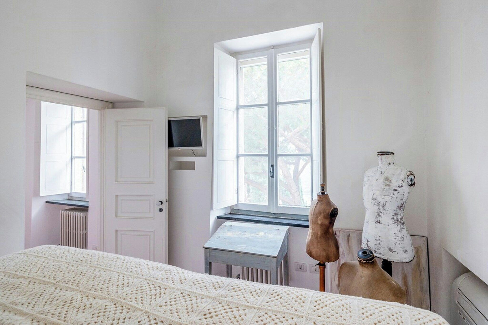 Una habitación con cama, ventana, televisor y un maniquí.