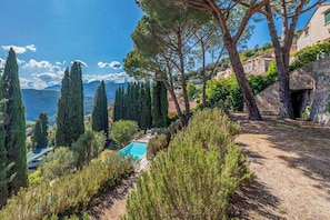 Ein Pool, umgeben von Zypressen, einer Steinmauer und Blick auf das Meer.