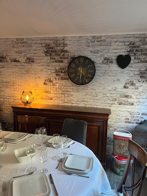 A dining area with a brick wall, a round table set for four, a clock, and a heart-shaped decoration.