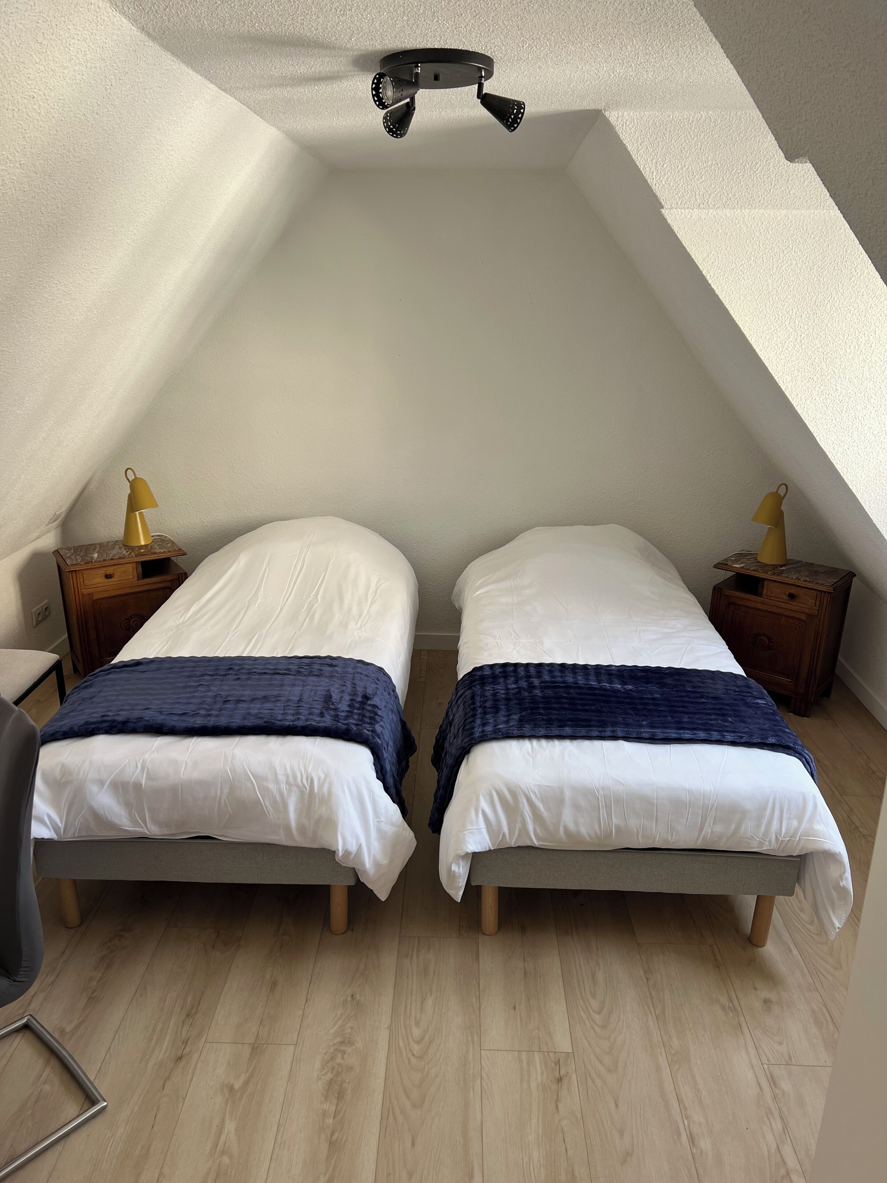 A room with two beds, wooden nightstands, a ceiling fan, and a chair.
