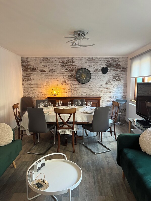 A dining area with a brick wall, a clock, and a television.