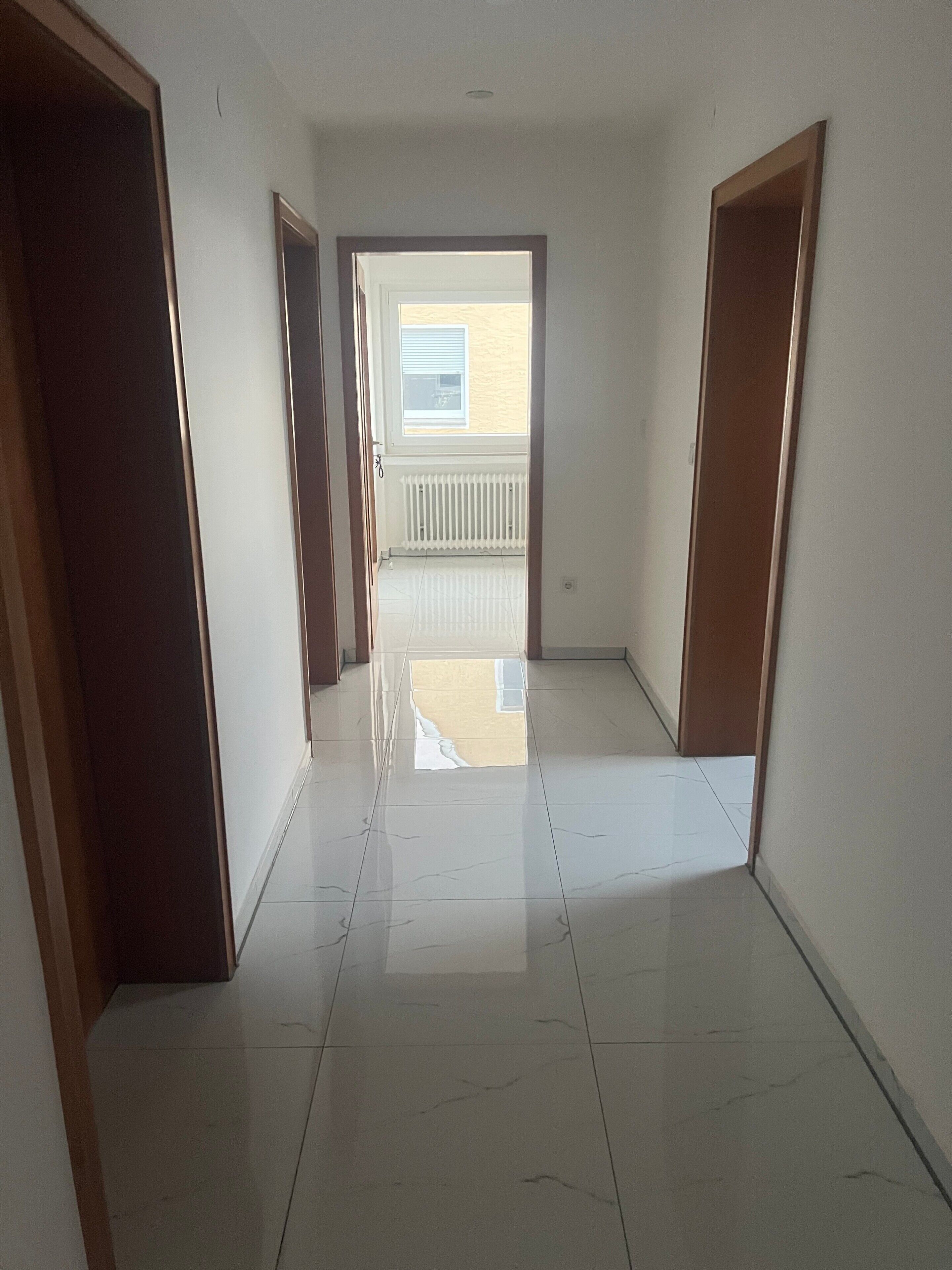 Um corredor com piso de azulejos que leva a uma varanda com corrimão branco.