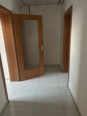 Ein Korridor mit einer Holztür, Fliesenboden in Weiß und schlichten Wänden.