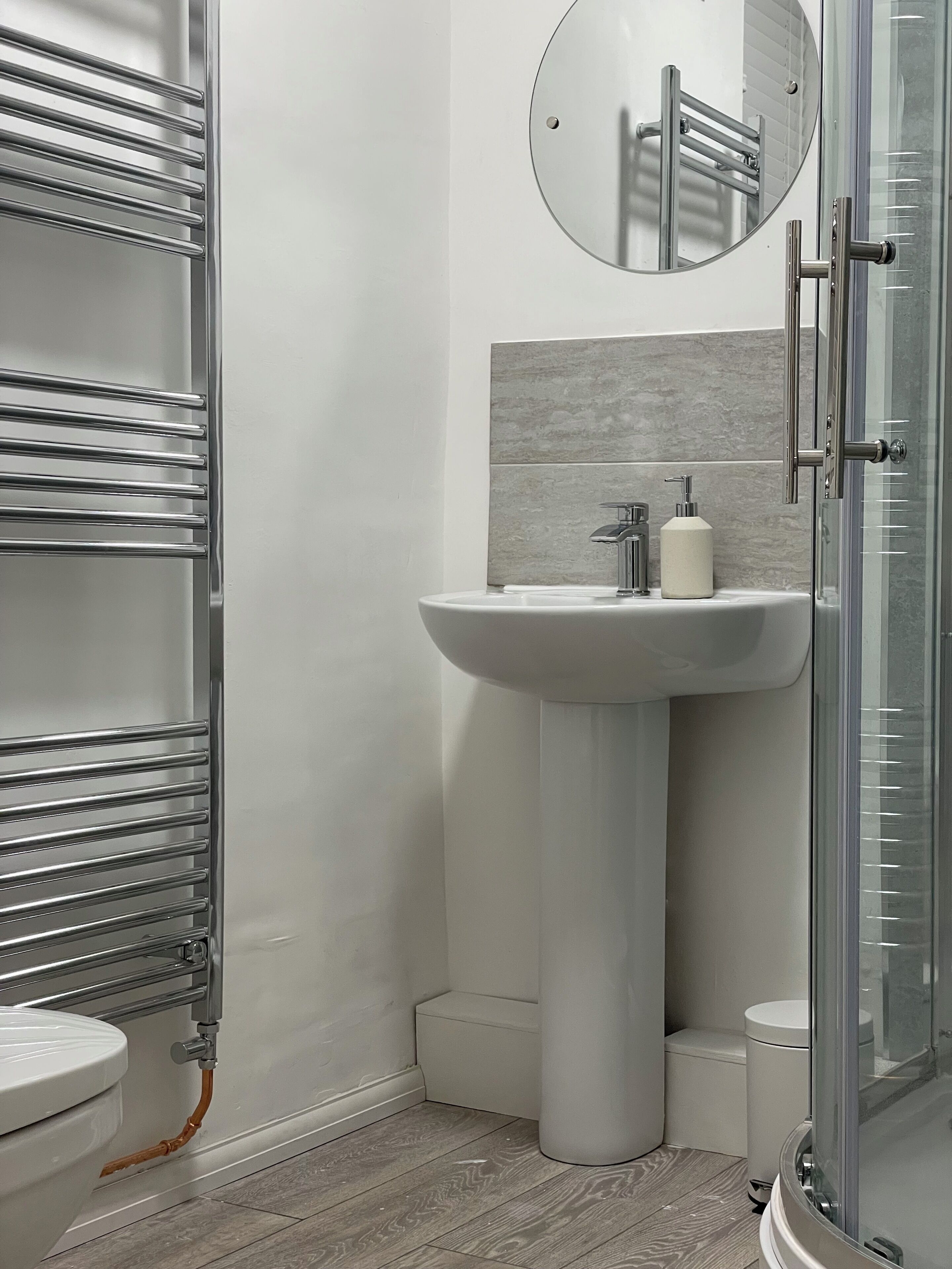 Un bagno moderno con box doccia in vetro, lavandino a colonna bianco e water.