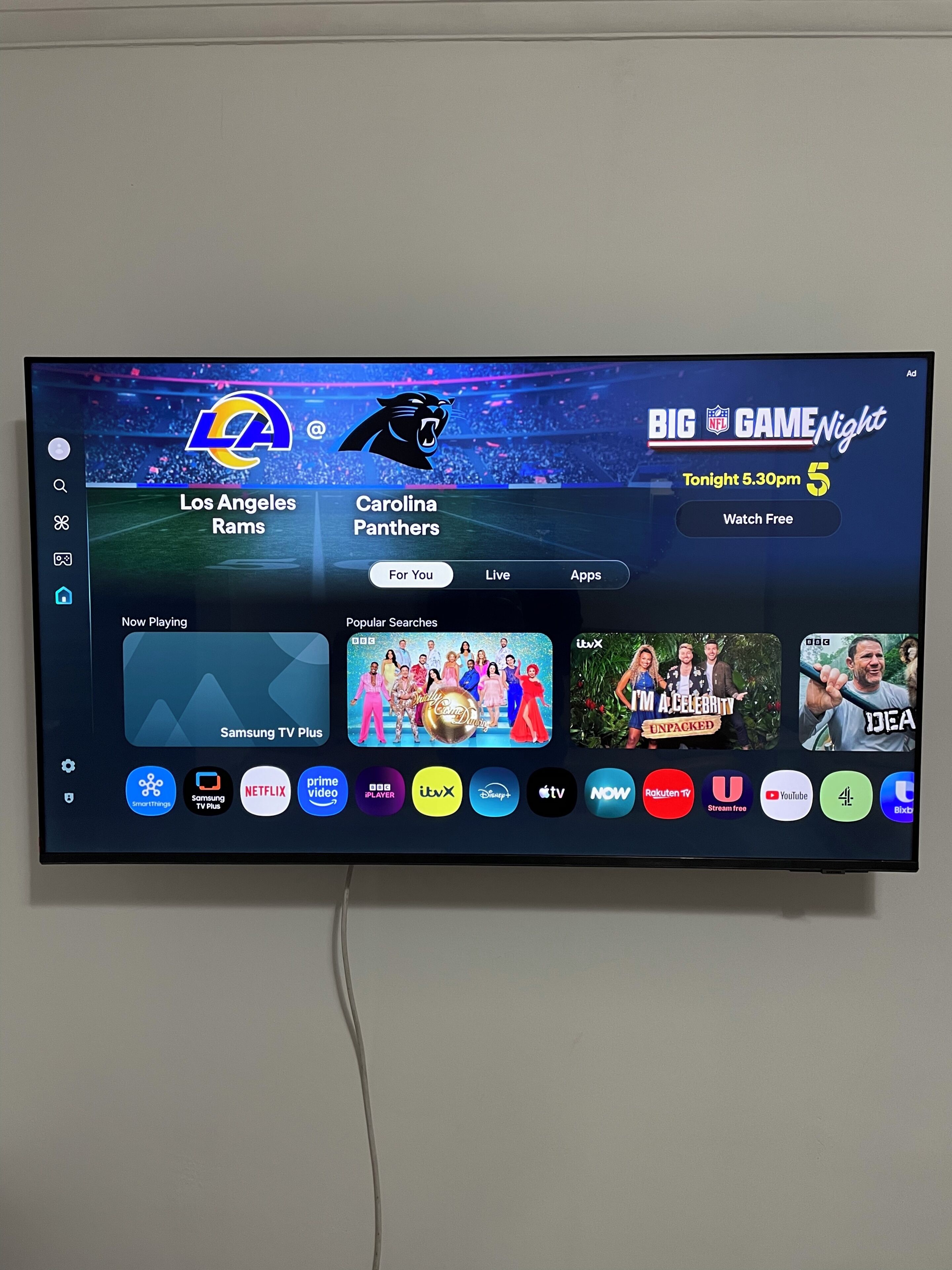 En tv-skärm som visar ett användargränssnitt för en sportkanal, med en fotbollsmatch mellan Los Angeles Rams och Carolina Panthers.