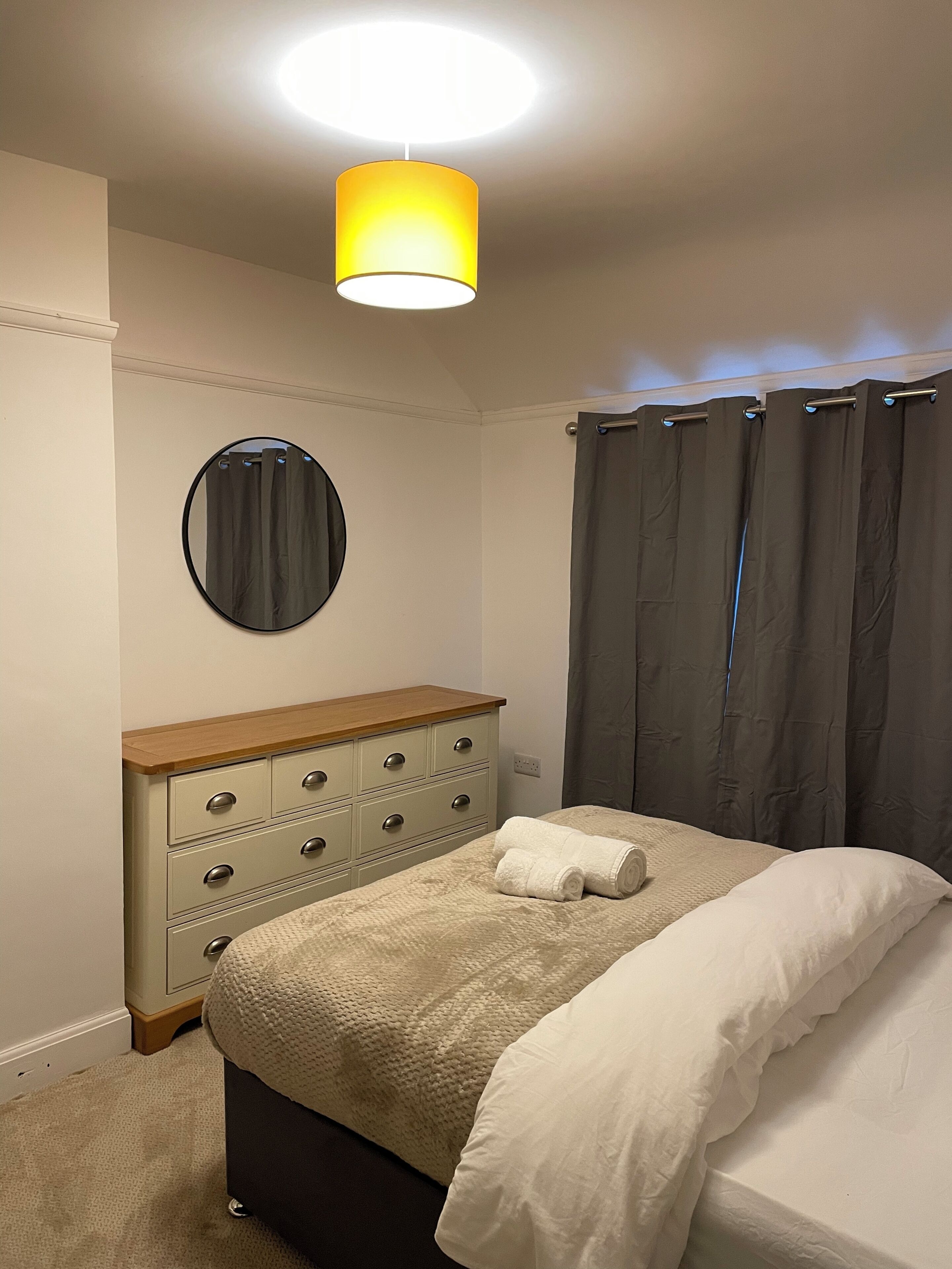 A bedroom with a bed, a dresser, a mirror, and a ceiling light.