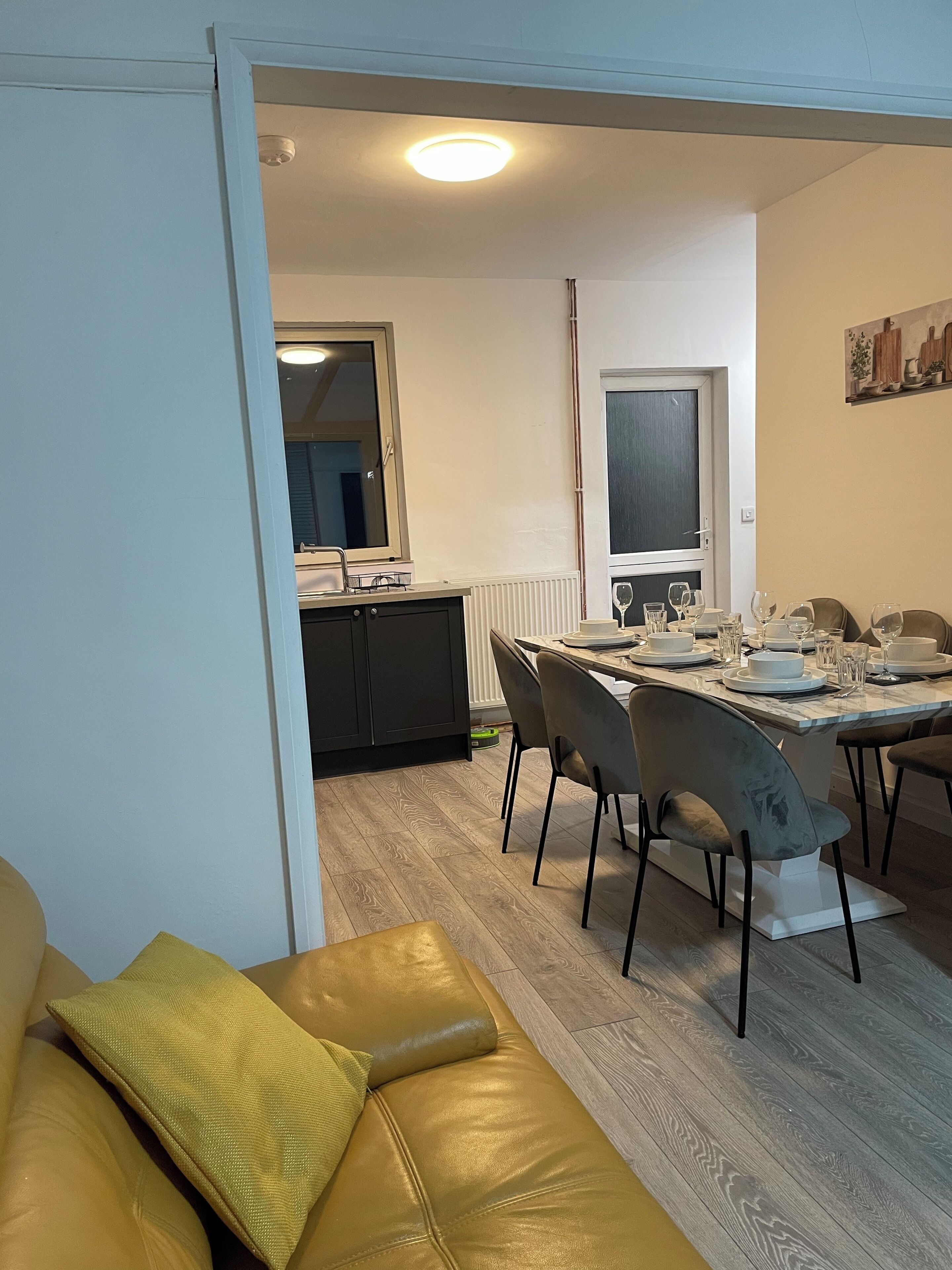 Un coin repas avec une table dressée pour quatre personnes, un canapé et une cuisine en arrière-plan.