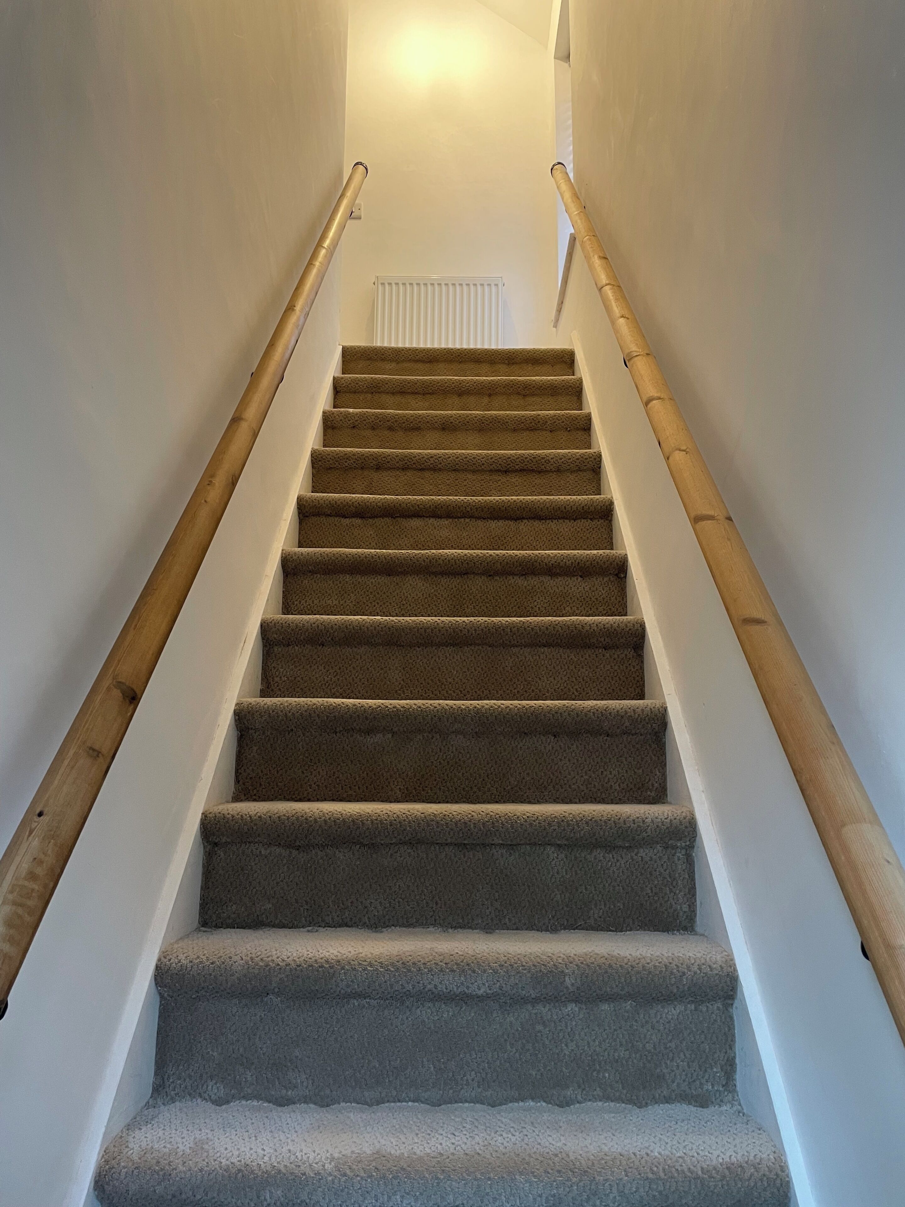 A carpeted staircase with wooden handrails, leading to a white radiator at the top.