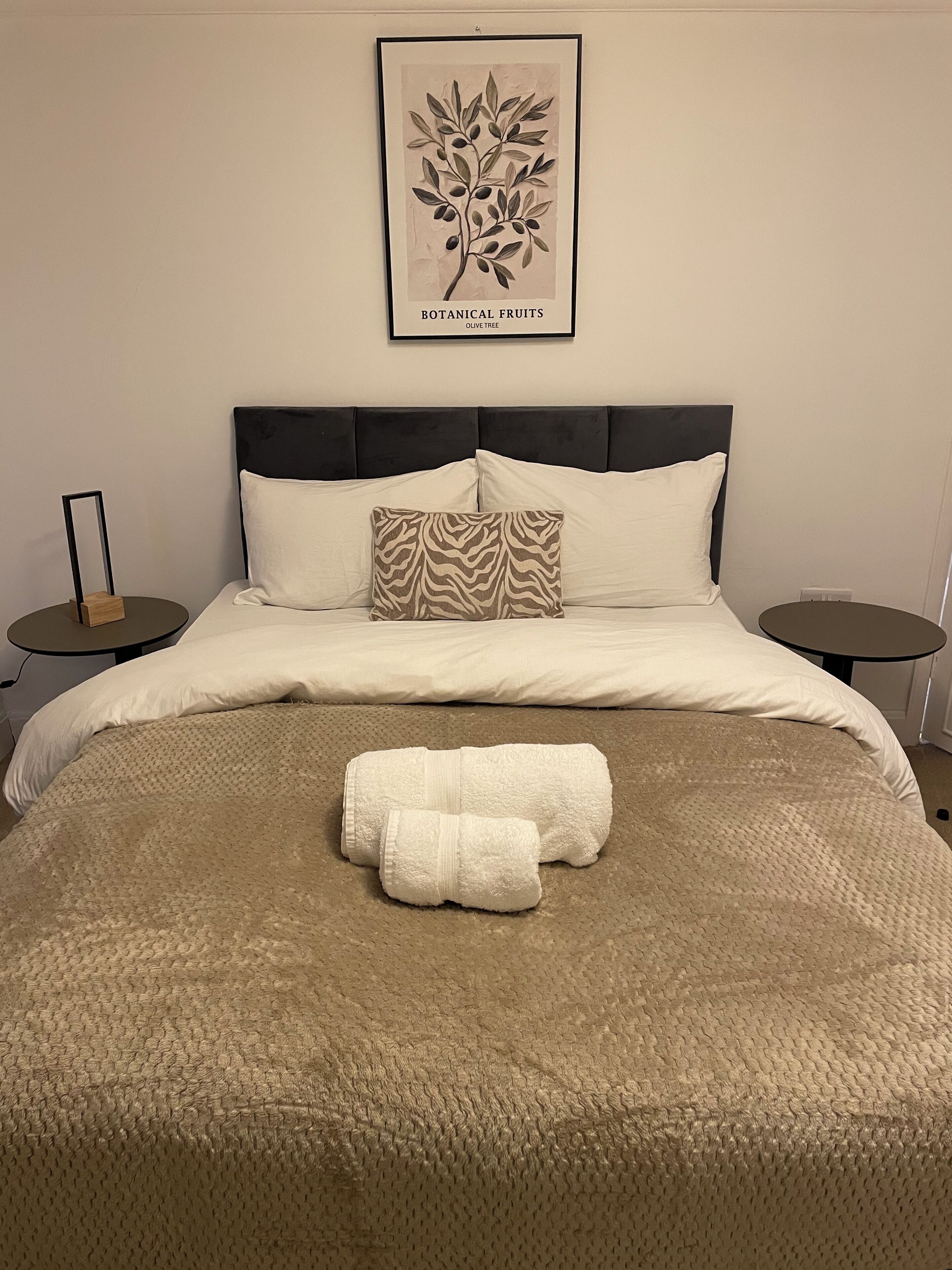 A neatly made bed with a textured blanket, two pillows, and a pair of towels.