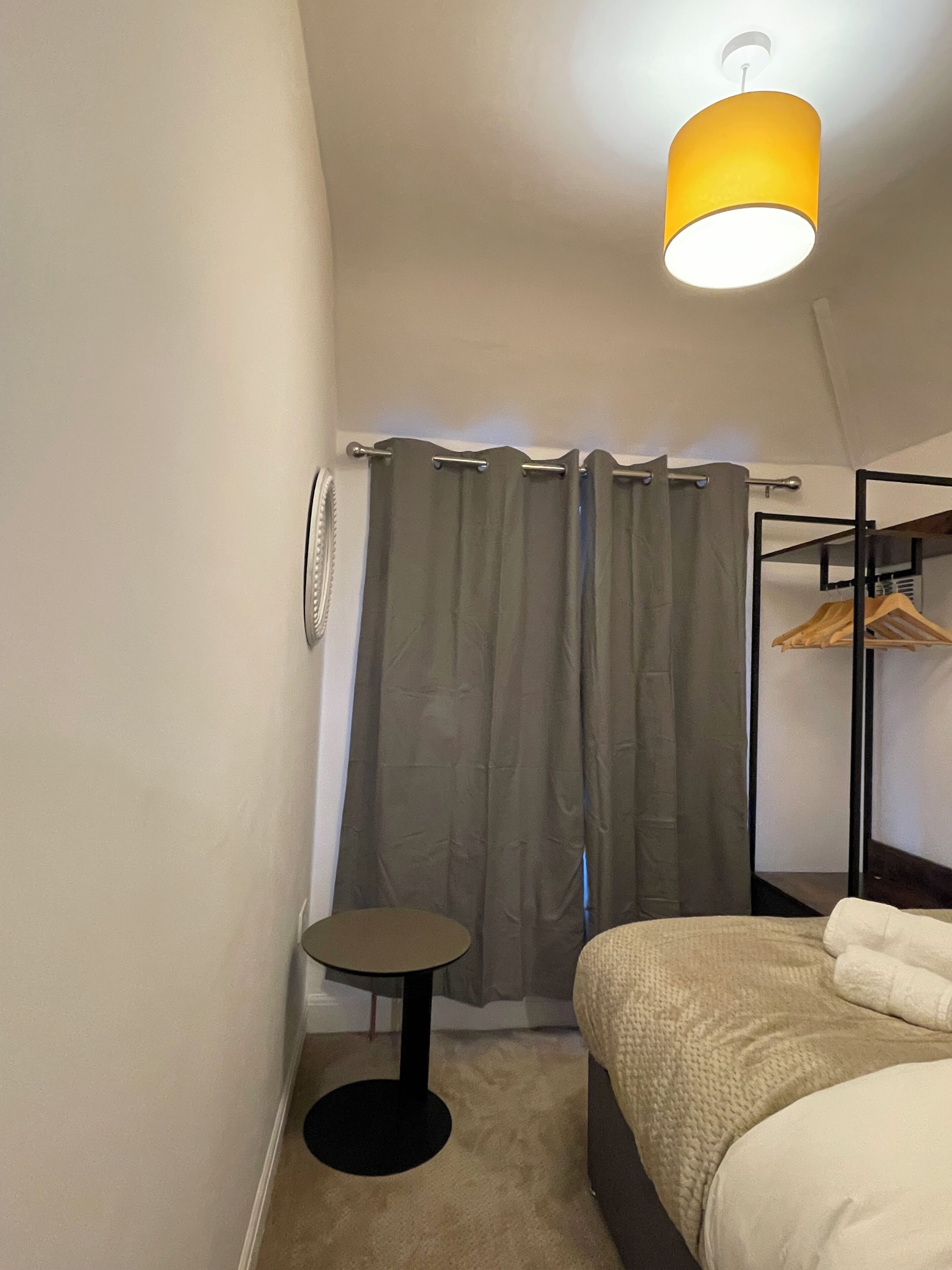 Une chambre à coucher avec un lit, une petite table ronde, un porte-vêtements suspendu et un ventilateur de plafond.