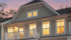 Ein zweistöckiges Haus mit Balkon, Garage und Veranda mit Beleuchtung.