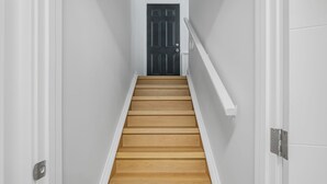 Eine Treppe mit Holzdielen und weißen Wänden, die zu einer dunklen Tür führt.