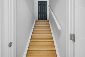 A staircase with wooden steps and white walls leading to a dark door.