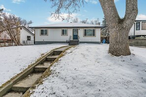 A single-story house with a front door, a small porch, and a snow-covered yard.