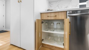 Eine Küche mit weißen Schränken, einem Edelstahlkühlschrank und einem Holzschrank mit Glasbehältern und Schüsseln.