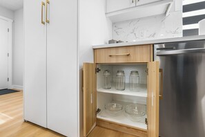 A kitchen with white cabinets, a stainless steel refrigerator, and a wooden cabinet with glass jars and bowls.