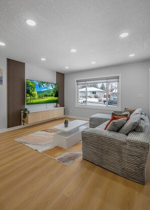 A modern living room with a flat-screen TV, a sofa, a coffee table, and a large window.
