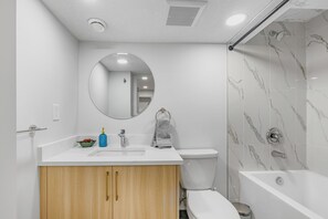 A modern bathroom with a white vanity, a round mirror, a toilet, and a shower area.